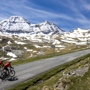 Cyclist riding on the scenic mountain road to Col de Tentes in the Pyrenees with snow-capped peaks background.